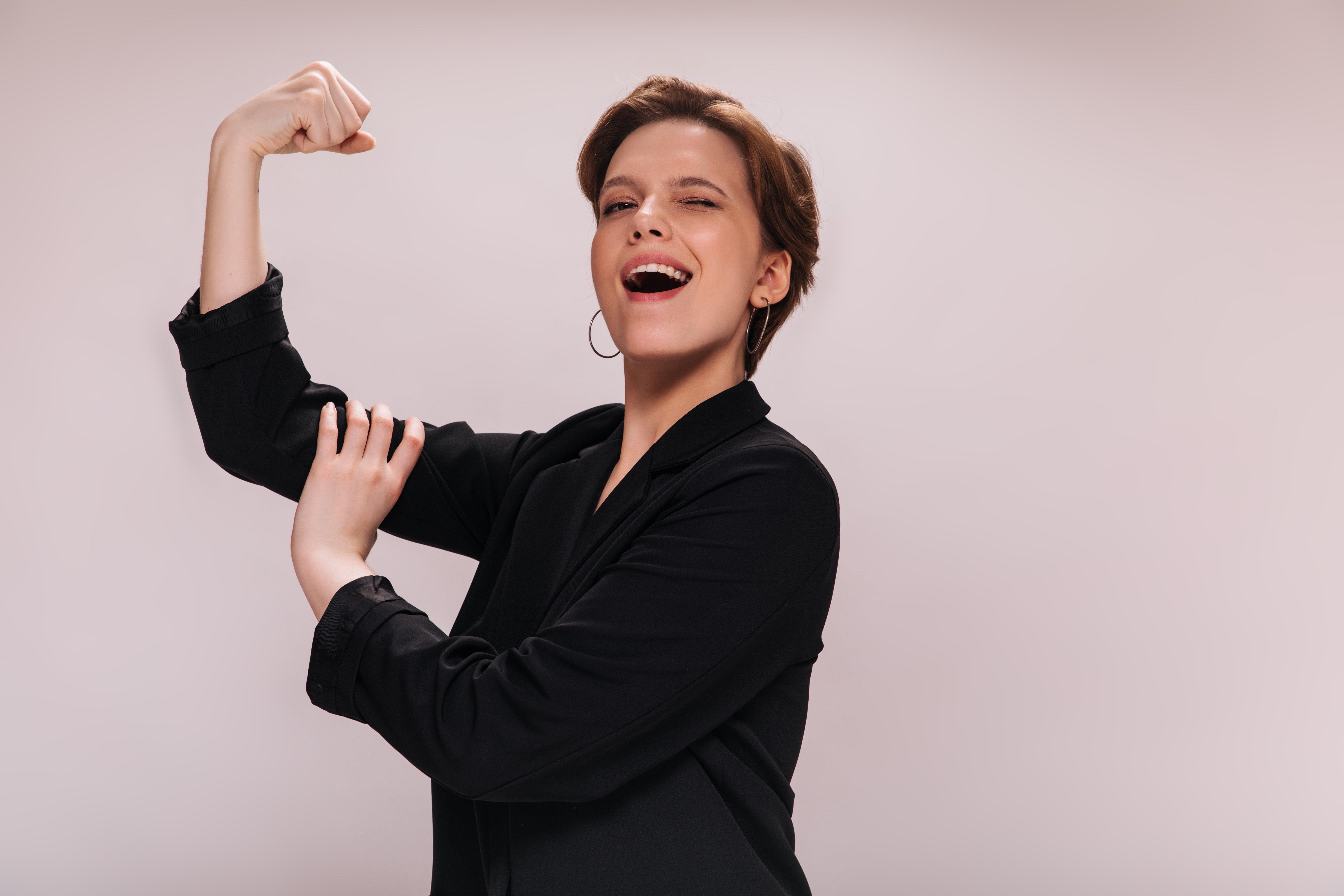 woman-rejoices-her-power-demonstrates-her-biceps-charming-lady-black-jacket-smiles-shows-muscles-isolated-background