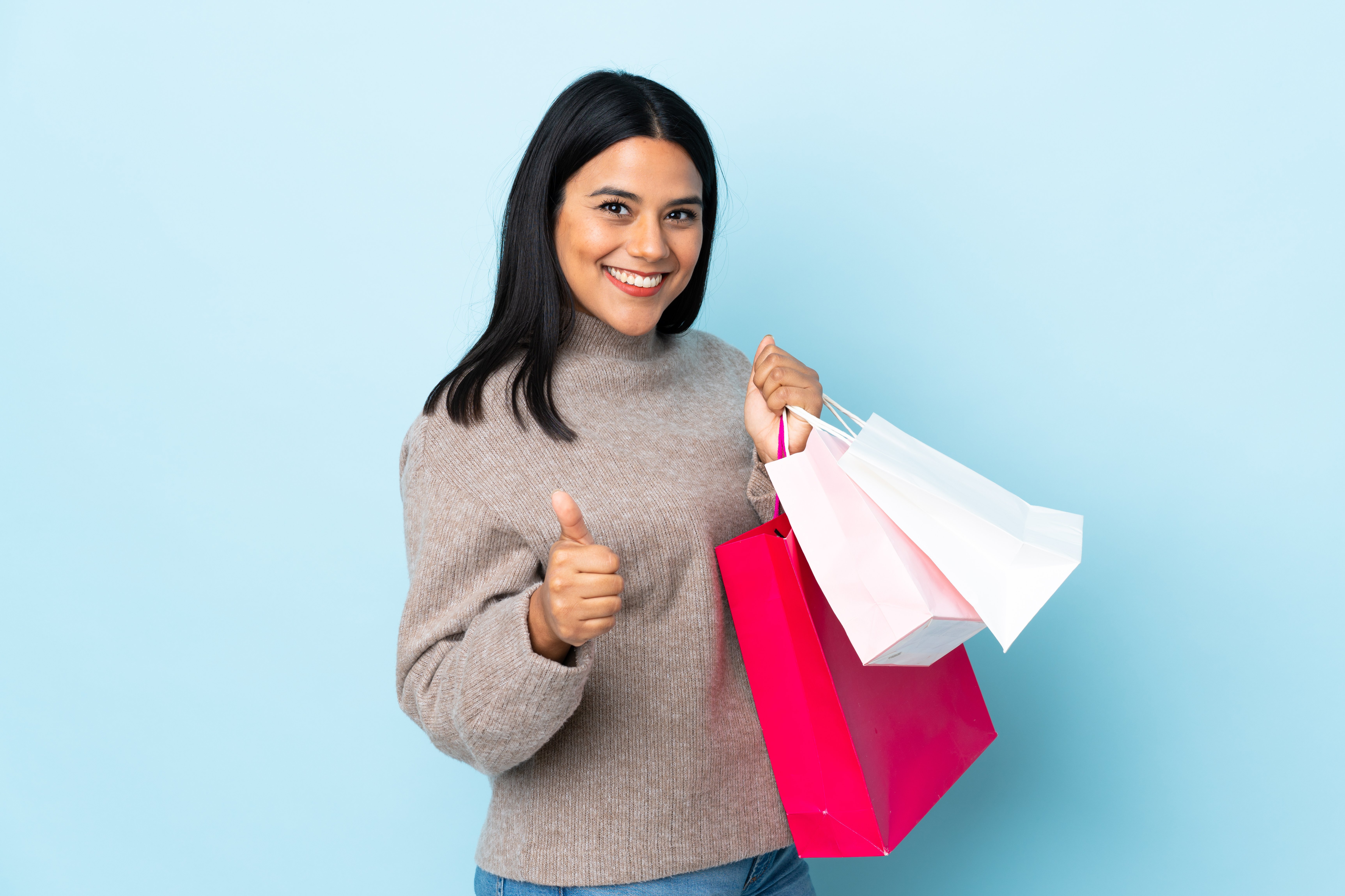 young-latin-woman-woman-isolated-on-blue-holding-shopping-bags-and-with-thumb-up